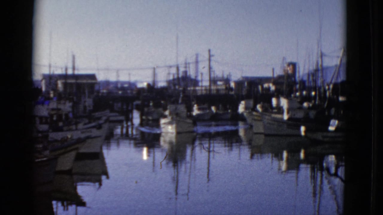 1952 San Francisco marina view with small boats, masts, dock pilings, and calm water reflections in an 8mm home-movie frame.