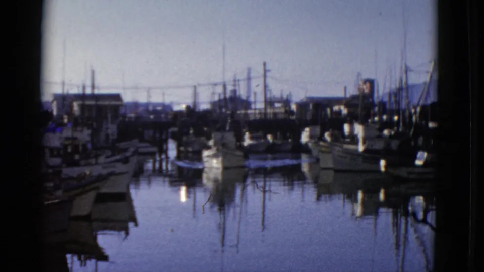 1952 San Francisco marina view with small boats, masts, dock pilings, and calm water reflections in an 8mm home-movie frame.