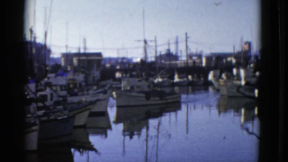 Soft 8mm view of a 1952 San Francisco harbor with moored vessels, dock structures, mast silhouettes, and blue-toned reflections.