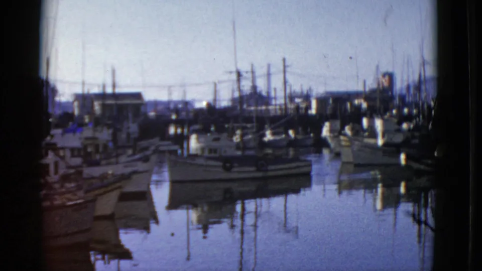 1952 San Francisco marina footage with a small fishing vessel among moored boats and dark pier edges.