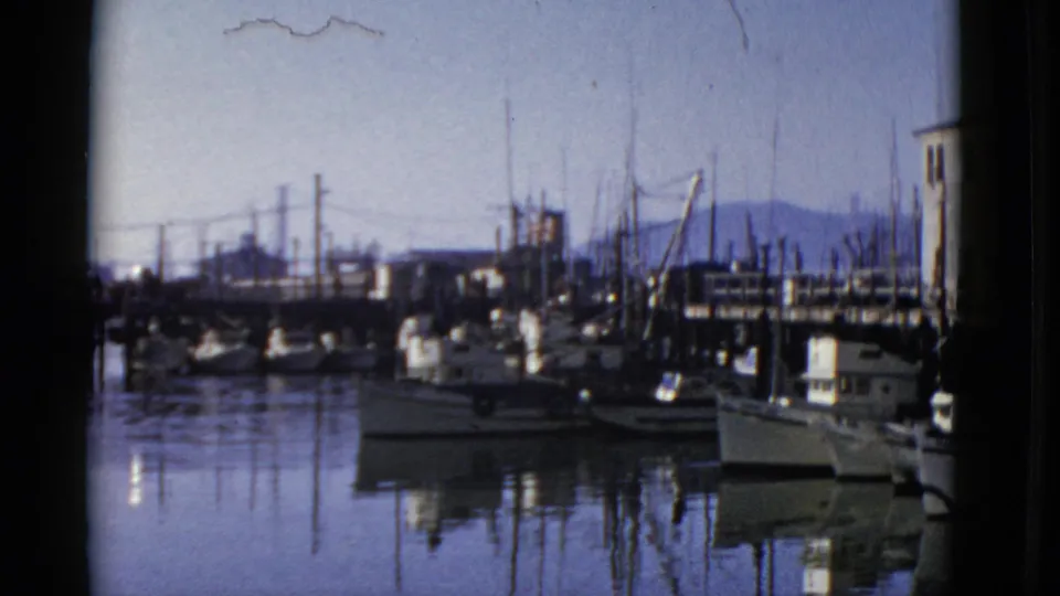 1952 San Francisco marina footage with sailboats along the dock, still water, utility poles, and a low waterfront skyline.