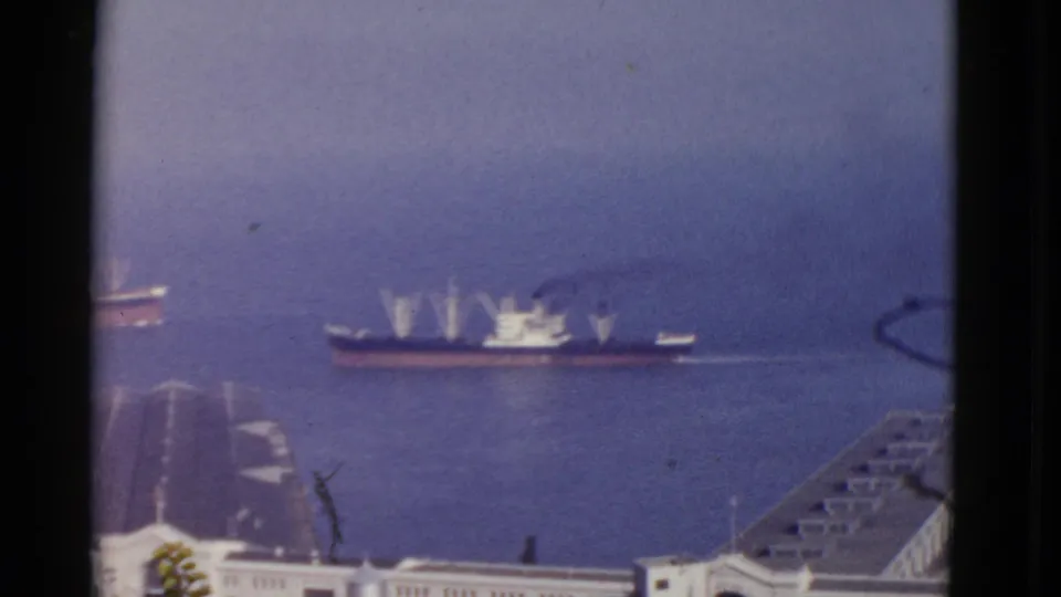 1952 San Francisco harbor view with large working ships crossing the water beyond docks, seen in soft 8mm color.