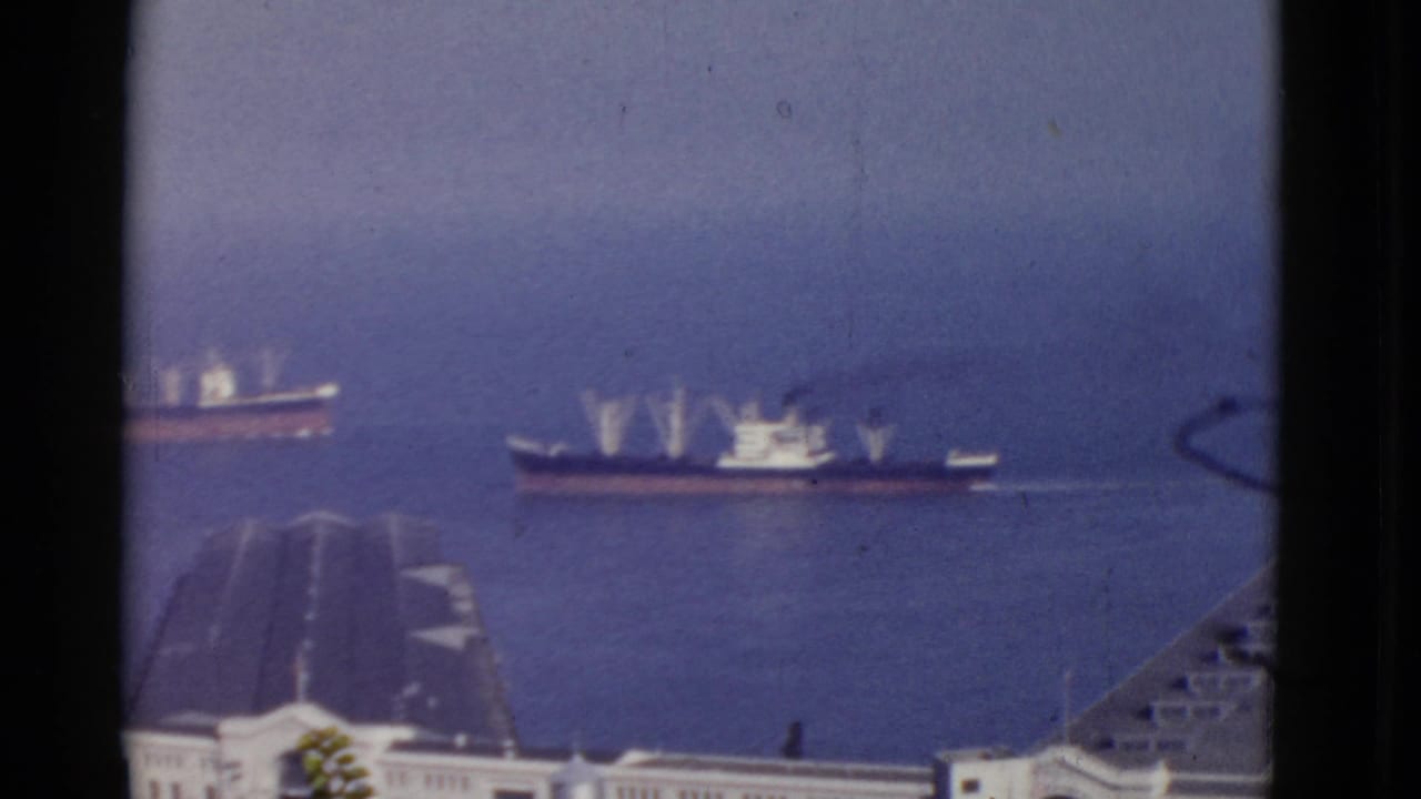 Cargo ships cross paths on open harbor water with pier structures in the foreground.