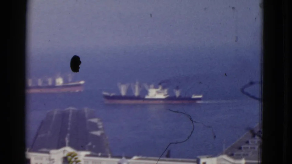 1952 San Francisco harbor frame with distant working ships, foreground dock structures, blue water, and visible dust on the 8mm scan.