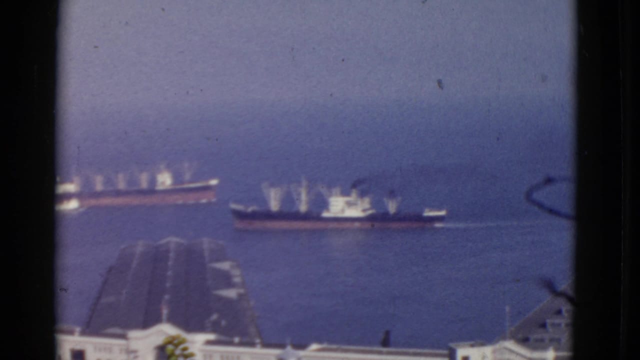 Two ships on a hazy bay seen above rooftops and dark frame borders.