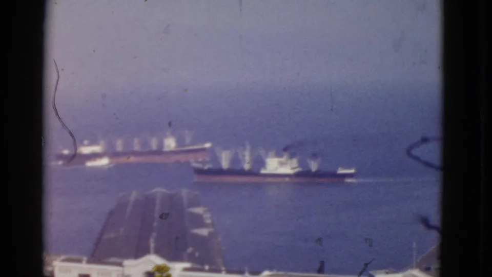 1952 San Francisco Bay home-movie frame showing distant ships on the water with rooftops below and visible film wear.