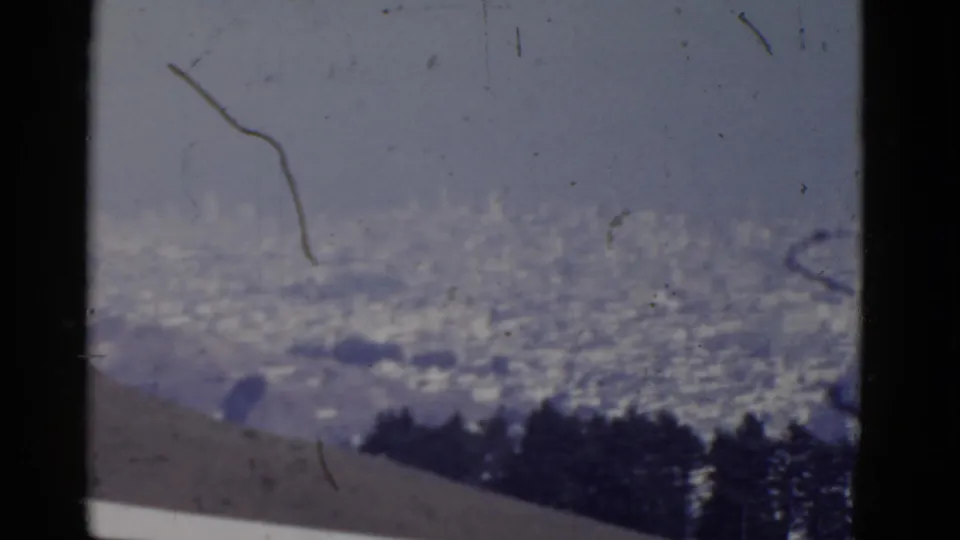 1952 San Francisco home-movie frame showing a soft-focus city vista beyond a hillside, with visible scratches and muted color.