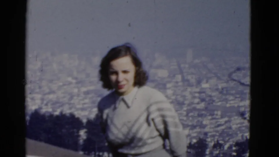 Closer 1952 home-movie frame of a woman at a San Francisco viewpoint, with a soft city grid behind her.