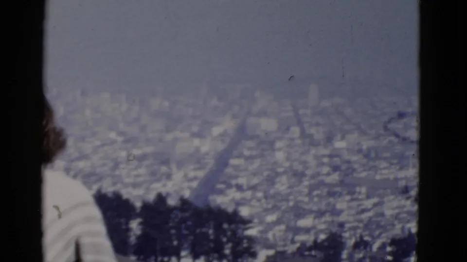 The woman moves partly out of frame while the San Francisco city view and dark tree line remain visible.