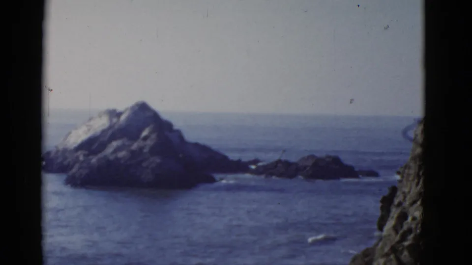 Vintage 8mm coastal frame from the San Francisco area showing an offshore rocky island, low outcrops, and calm ocean water.