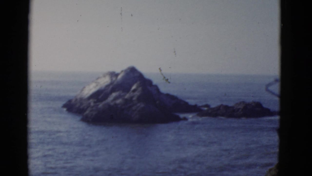 Offshore rock formation with ocean and pale sky, framed by black film edges.