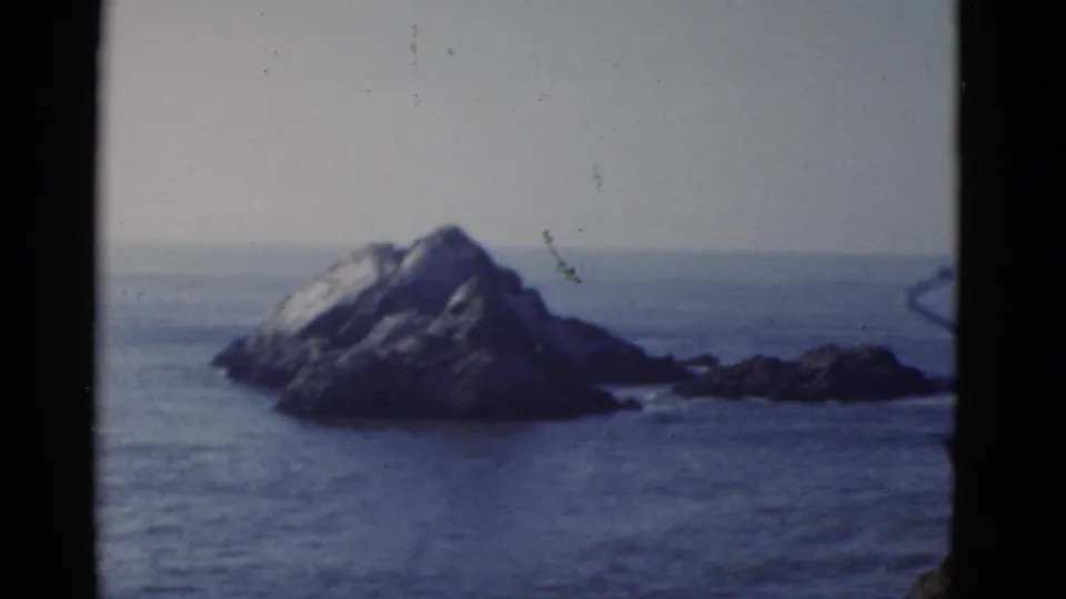 1952 San Francisco-area coastal view with a rocky island or sea stack, calm ocean surface, pale sky, and visible film wear.