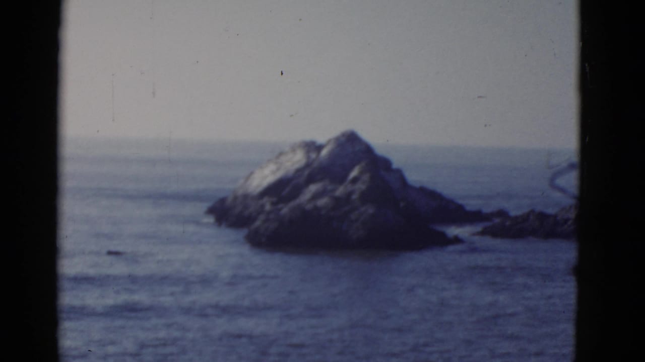 1952 8mm frame of large coastal rocks in water near San Francisco, with soft focus, faded color, and visible film borders.