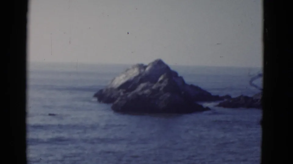 1952 8mm frame of large coastal rocks in water near San Francisco, with soft focus, faded color, and visible film borders.