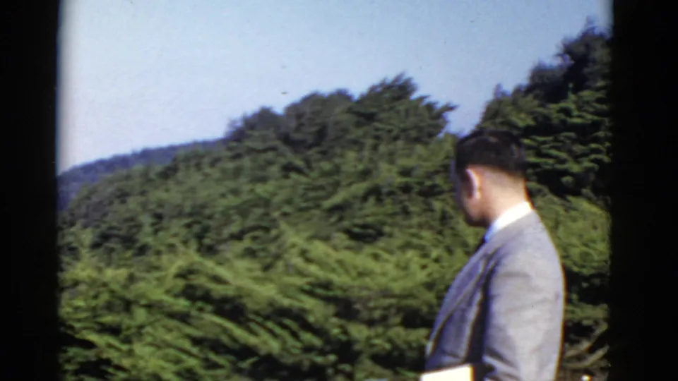 A suited adult man looks away across a green coastal landscape in this 1952 San Francisco-area home-movie frame.