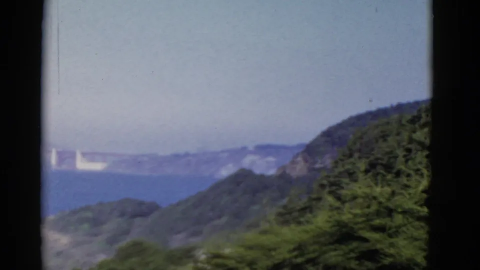 The Golden Gate Bridge appears faintly across San Francisco Bay, framed by green hillside vegetation and hazy distant shoreline.