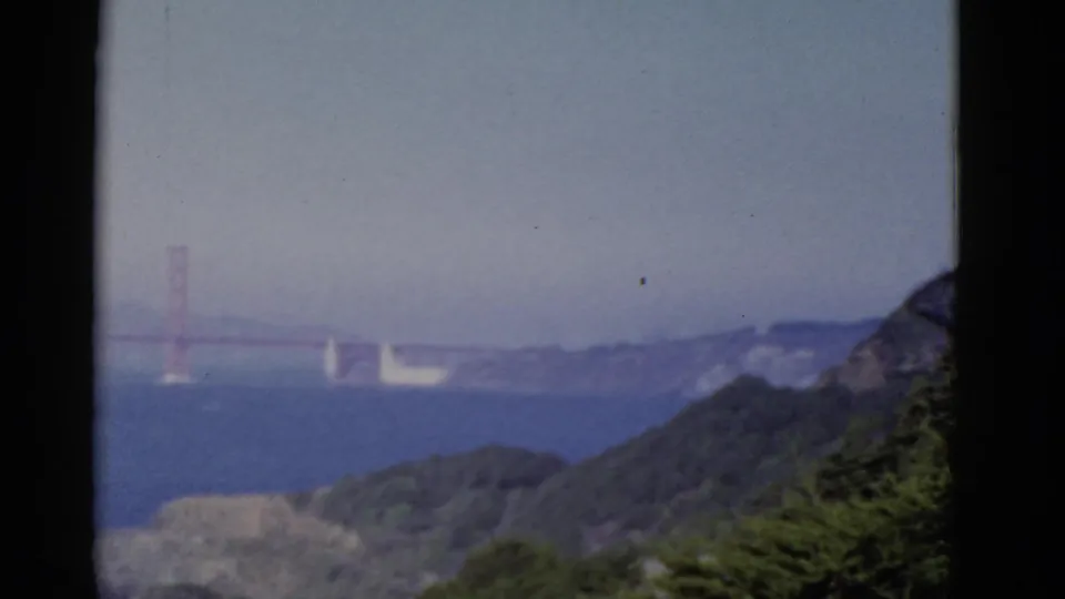 A hazy 1952 view across San Francisco Bay shows the Golden Gate Bridge, blue water, wooded hills, and a pale sky.