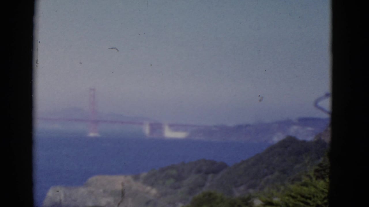 1952 San Francisco 8mm frame showing the Golden Gate Bridge in soft focus beyond bay water and foreground hills.