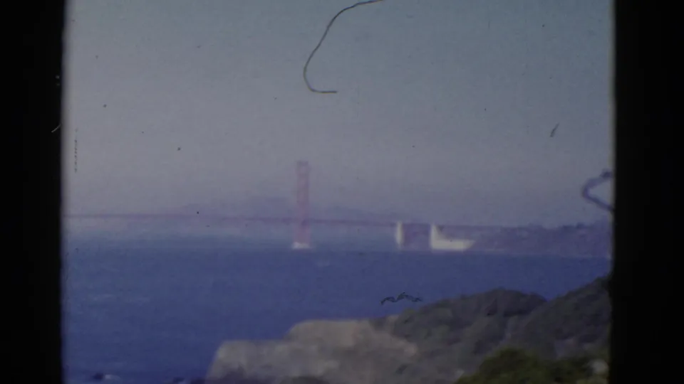 1952 San Francisco home-movie frame with the Golden Gate Bridge spanning the hazy bay beyond dark hillside foreground.