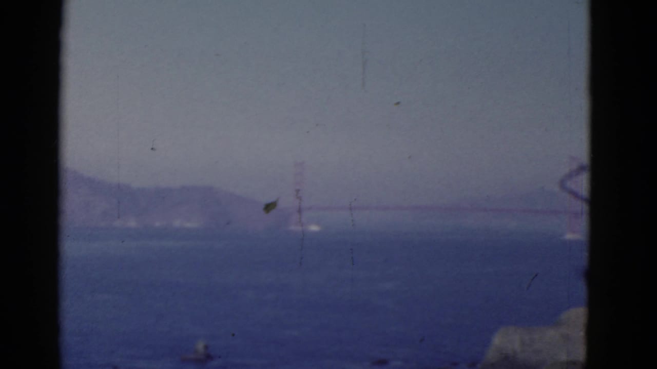 A 1952 San Francisco home-movie frame shows the Golden Gate Bridge faintly visible across the bay in atmospheric haze.