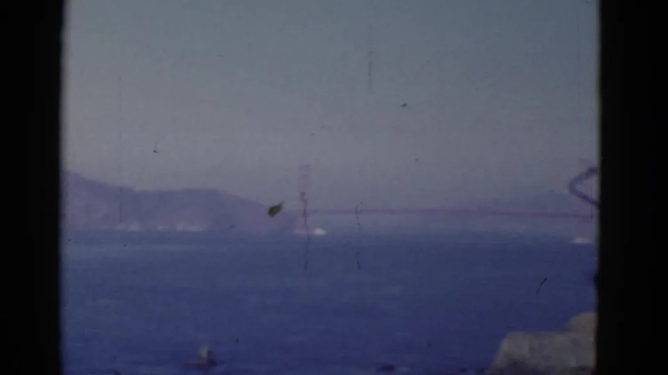 A 1952 San Francisco home-movie frame shows the Golden Gate Bridge faintly visible across the bay in atmospheric haze.