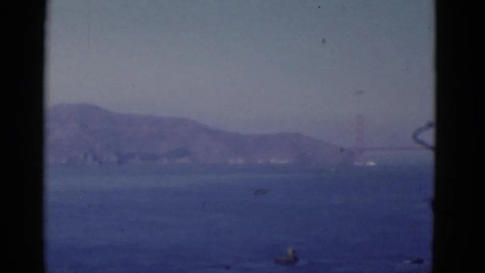 A hazy San Francisco bay view frames the Golden Gate Bridge tower and distant shoreline in soft 8mm color.