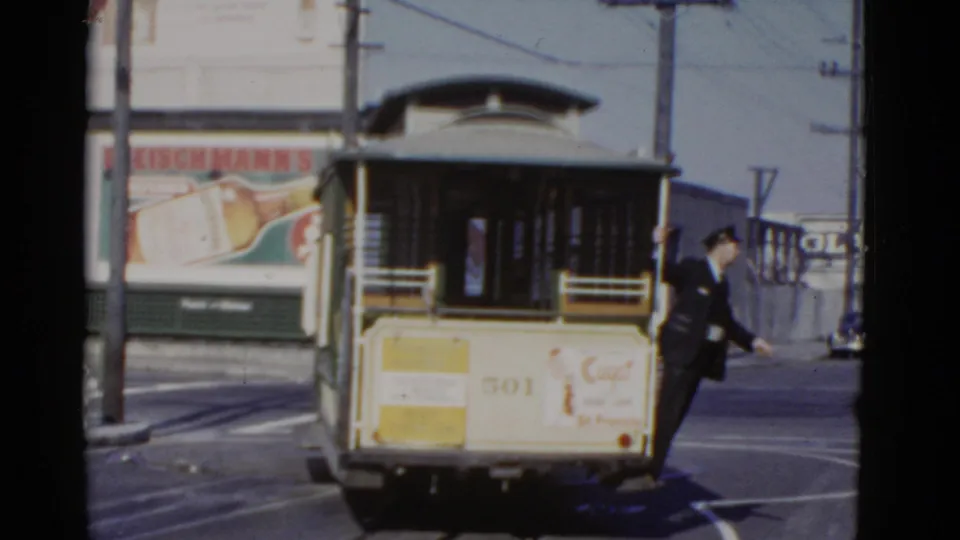 The rear of San Francisco cable car 501 appears on a street while a uniformed man stands or steps beside the car.