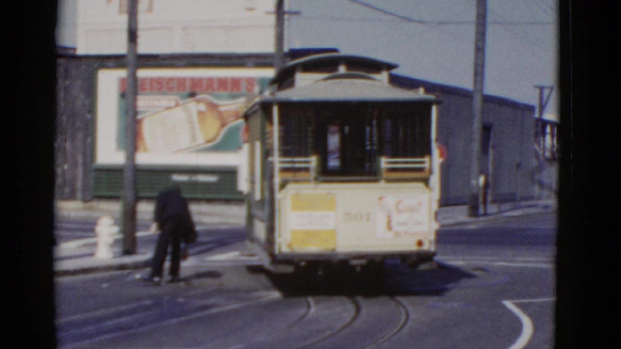 1952 San Francisco streetcar viewed from behind on a city street, with rails, overhead wires, a pedestrian, and a large beer billboard visible.