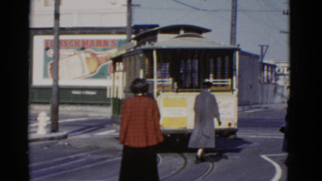 Two pedestrians approach a streetcar from behind as it moves along curved tracks.