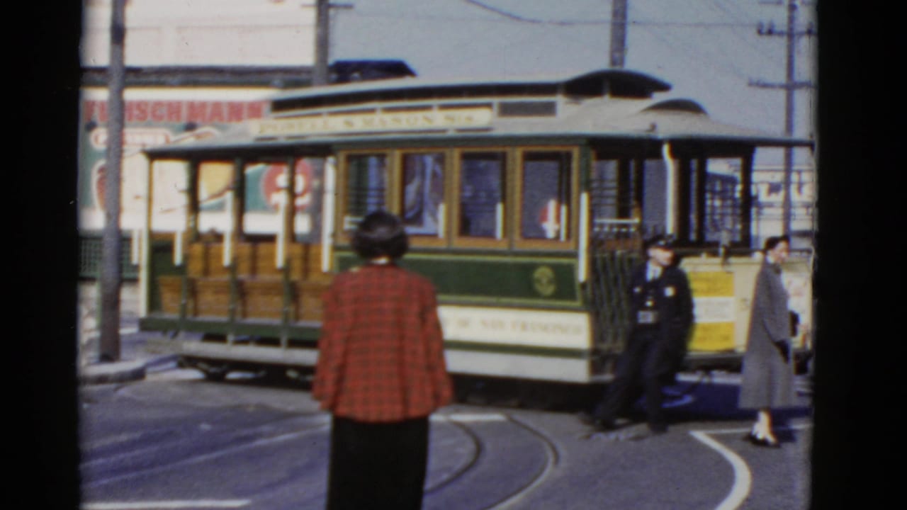 The cable car moves through the street turn while pedestrians and overhead wires frame the 1952 San Francisco scene.