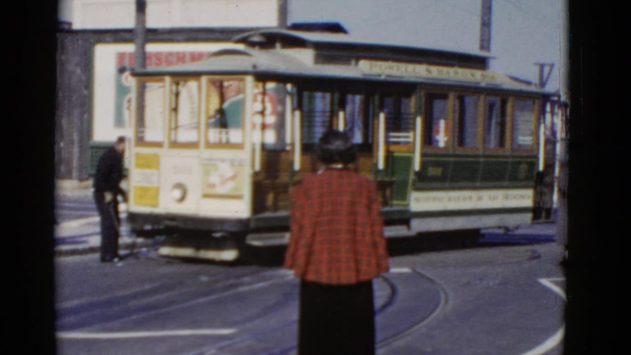 Cable car turns along street rails with pedestrians nearby.