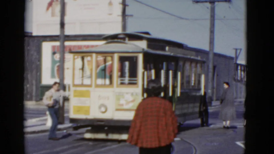1952 San Francisco cable car front is centered while pedestrians stand near the rails and a woman in red plaid is seen from behind.