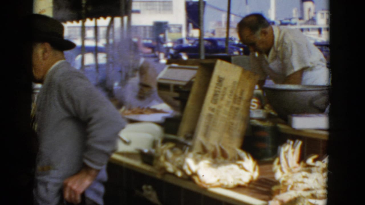 1952 San Francisco waterfront crab stand with a suited man in a fedora near steaming crabs and a vendor behind the counter.