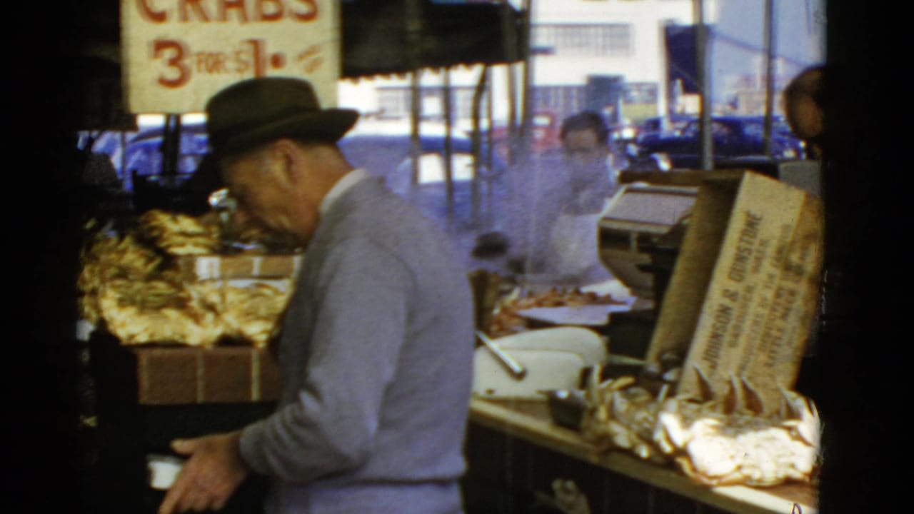 Fedora-wearing customer stands beside crab displays under a large crabs price sign.