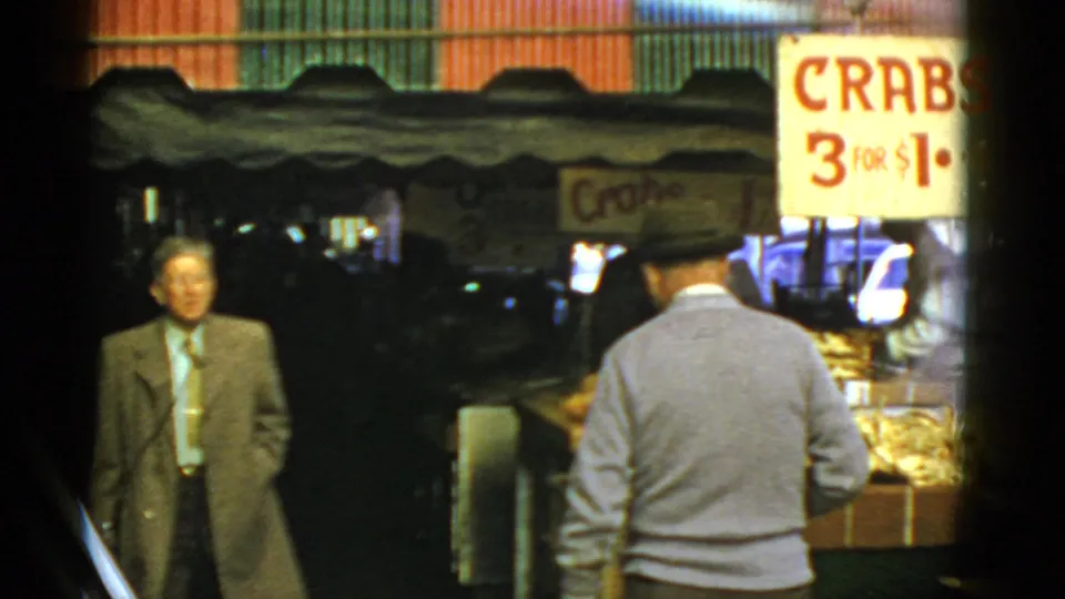 A suited man enters the market scene while the man in a sweater faces the crab display beneath the red-and-white sign.