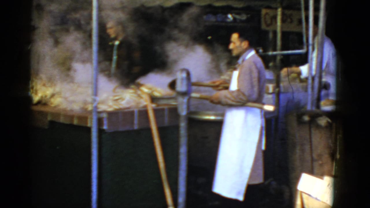 Aproned vendor tends steaming pots beside a market stall counter.
