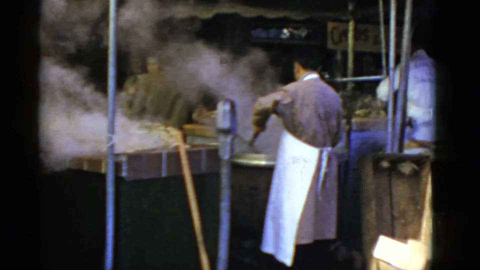 San Francisco market vendor in a white apron works with steaming crab pots, seen from behind in 8mm home-movie footage.