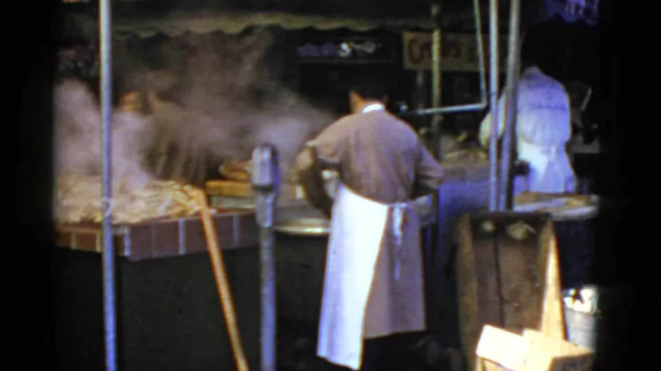 1952 San Francisco street-market view of an aproned worker bending over steaming crab pots near a seafood counter.