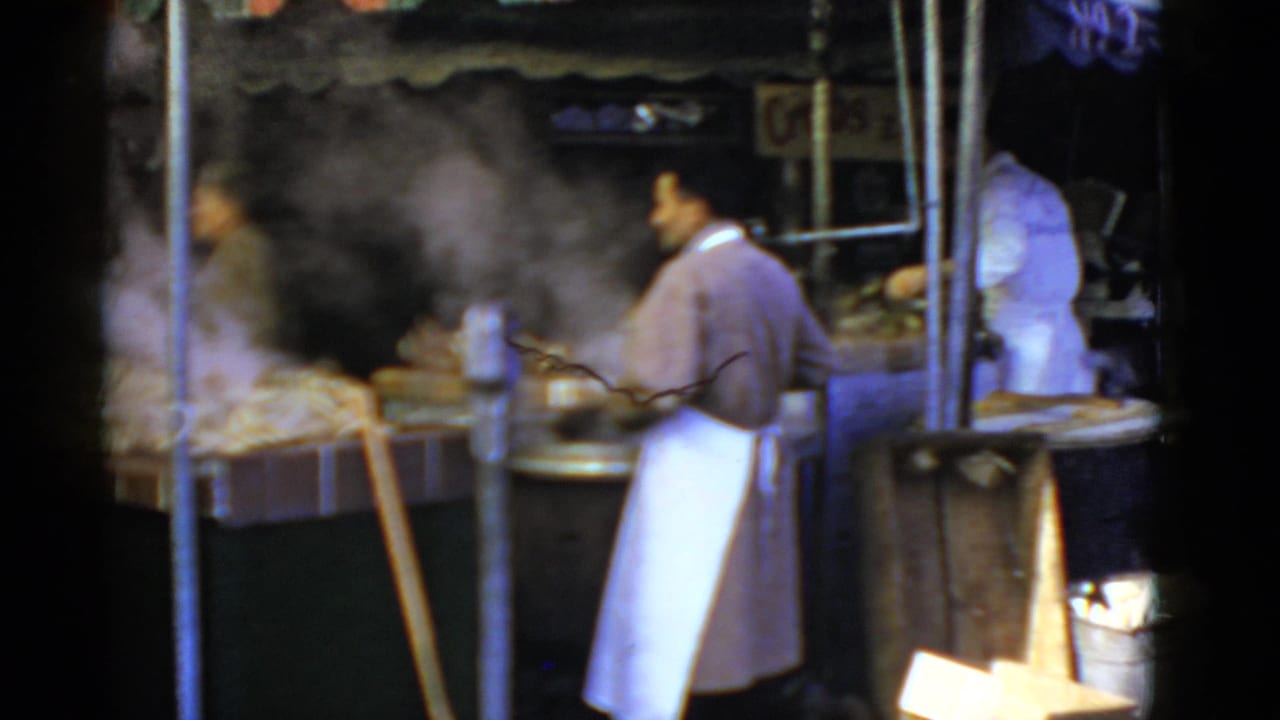 1952 San Francisco home-movie frame showing workers in white aprons at a steaming sidewalk food stall.