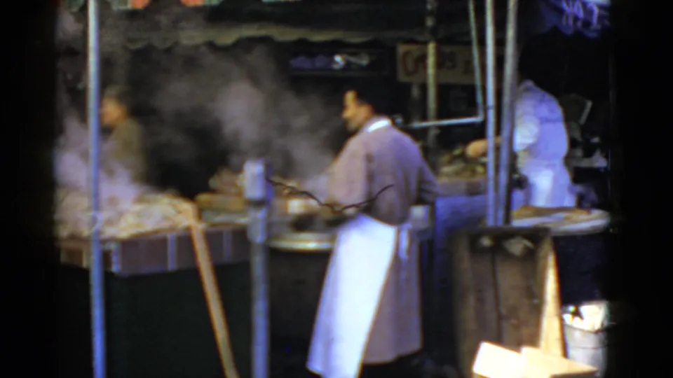 1952 San Francisco home-movie frame showing workers in white aprons at a steaming sidewalk food stall.