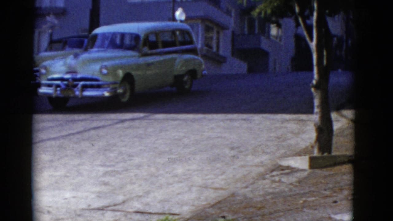 Light-colored station wagon parked or moving along a sunlit street.