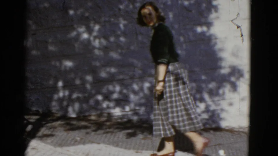 Near the end of the 1952 San Francisco clip, the woman slows near a wall where foliage shadows fall across the sidewalk.