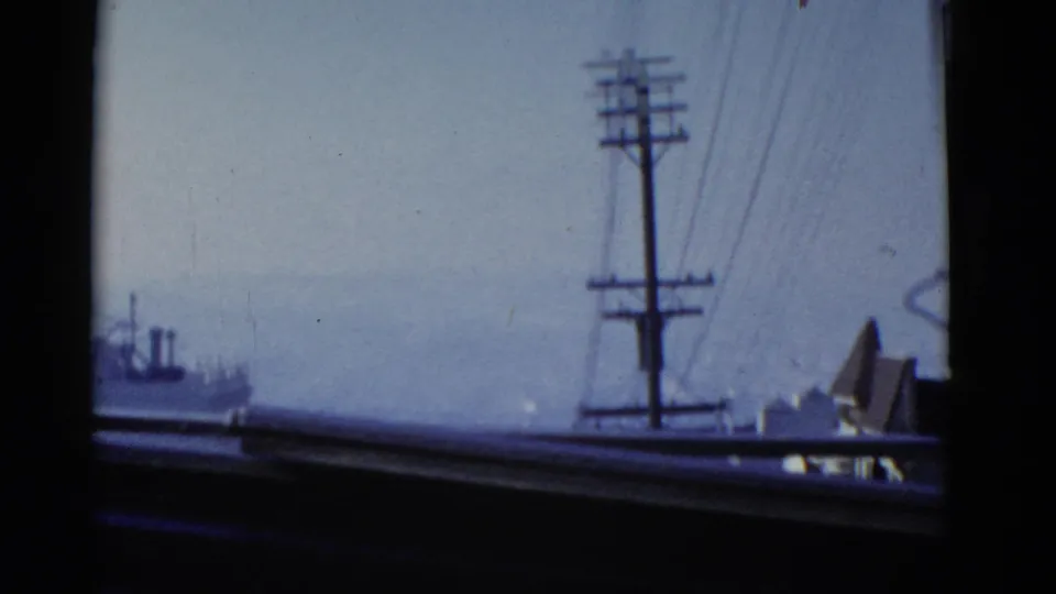 Hazy San Francisco view with utility pole, wires, rooftops, and a distant waterfront or ship shape in soft 8mm color.