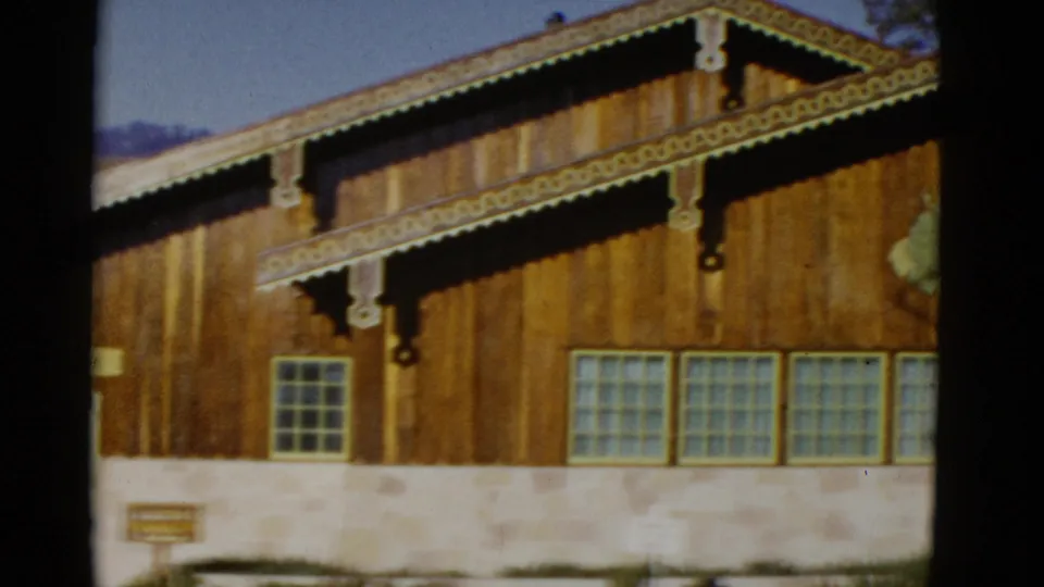 1952 8mm frame during a pan across the chalet-style post office, focusing on the wood siding, ornamental trim, stone base, and window row.