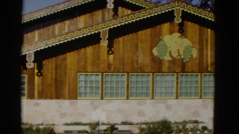 End of the 1952 home-movie pan across the rustic post office exterior, showing ornamental trim, a painted tree motif, windows, and stone foundation.