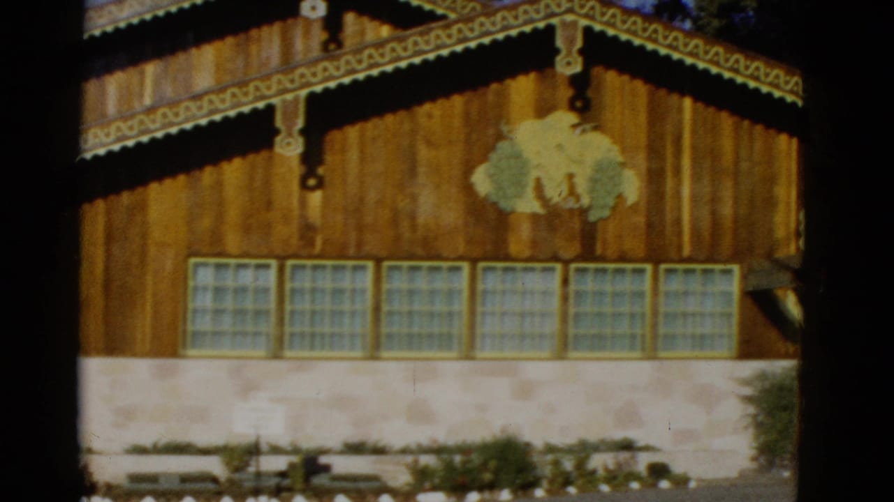 1952 home-movie frame showing a rustic wooden building facade with decorative trim, glass-block windows, and a stone base.
