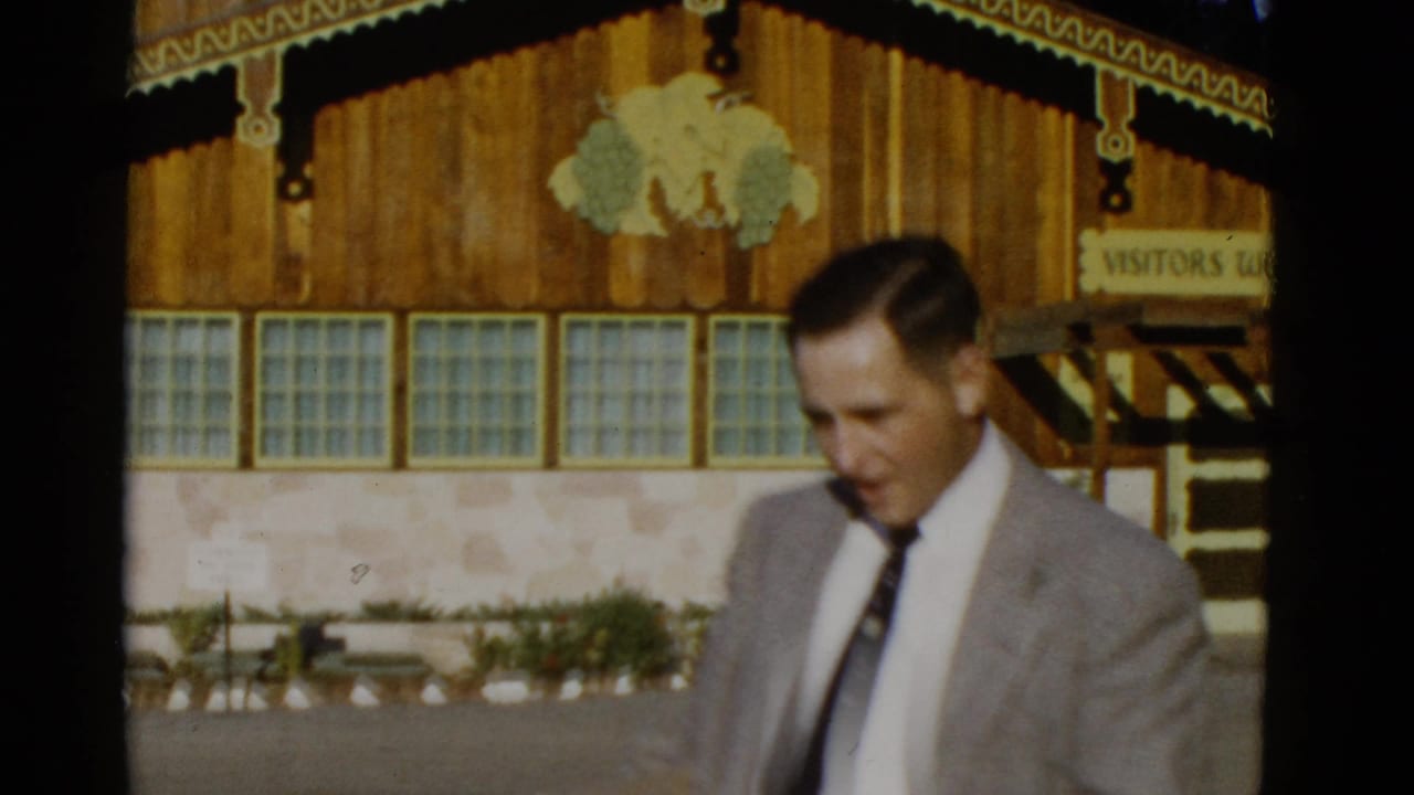 Man in a light gray suit walks in front of a wooden visitor entrance.