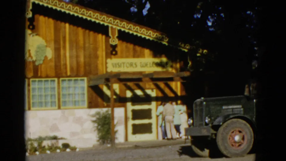 The visitor entrance is seen with several people near the doorway, a visible sign, glass-block windows, and a parked vintage truck.