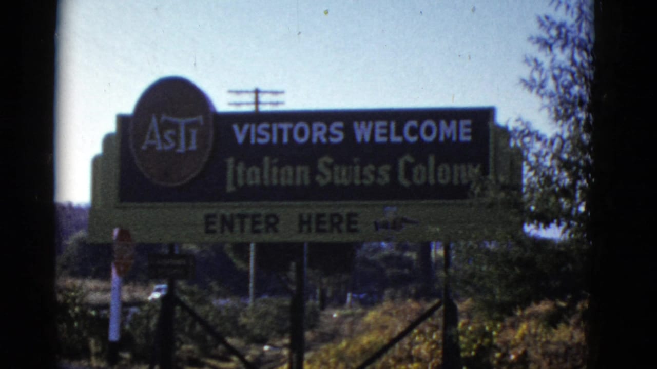 Large roadside sign reading visitors welcome for Italian Swiss Colony with fencing below.