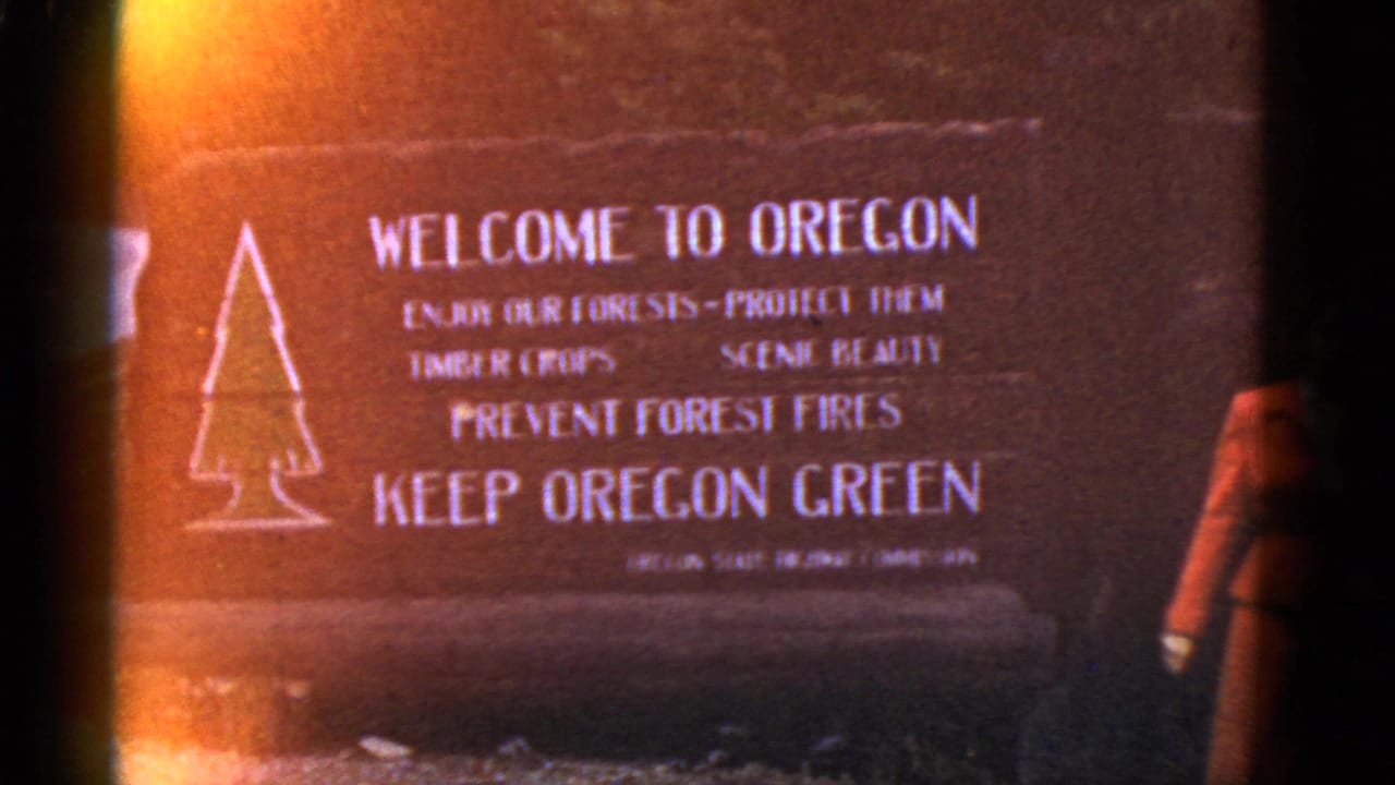 Warm-toned 8mm frame showing the Welcome to Oregon sign and a cropped woman beside it.